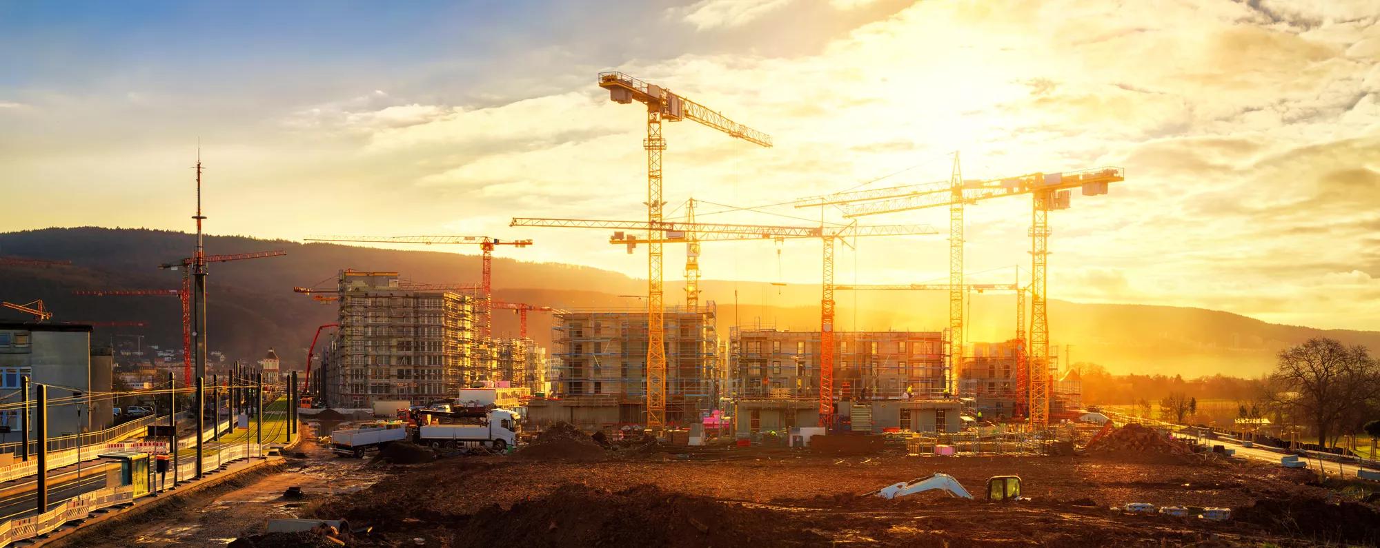 Large construction site including several cranes working on a building complex, illumined by warm gold sunlight