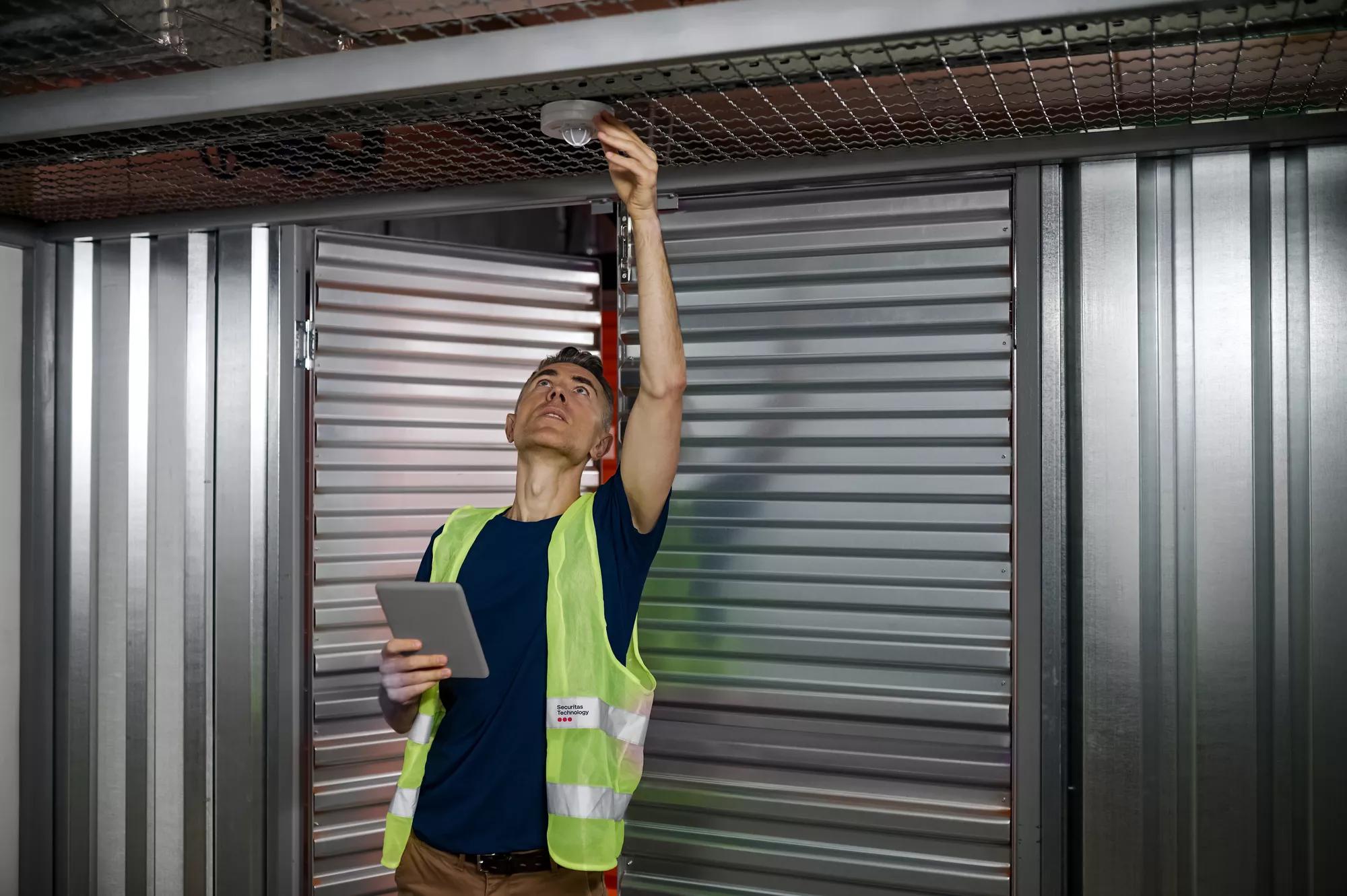 Fire alarm. Serious focused responsible man with tablet checking fire safety adjusting device on garage ceiling