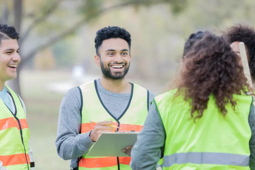 Confident young man talks with a group of male and female community volunteers. He is giving them instructions. They are wearing safety vests.