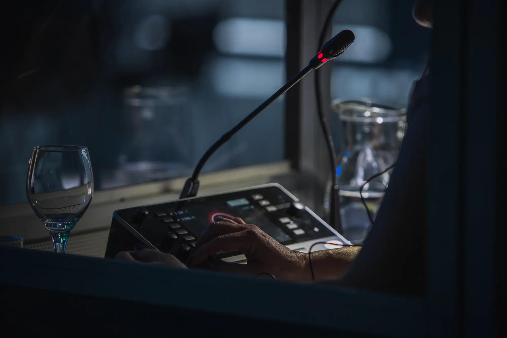 Translator or translation booth at a conference. Hand of a person for simultaneous translating is seen working in a booth. Glass of water next to a translator.