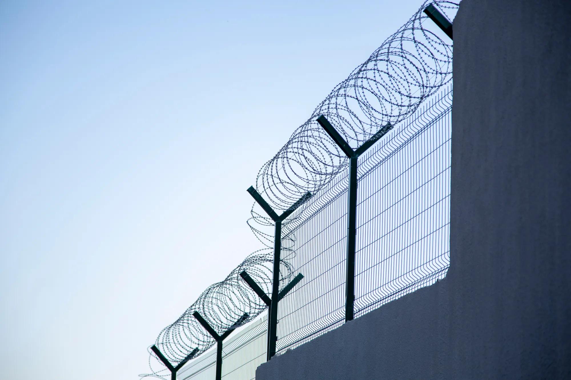 Steel grating fence of soccer field,Metal fence wire with bokeh in the background . Coiled razor wire with its sharp steel barbs on top of a wire mesh perimeter fence ensuring safety and security.