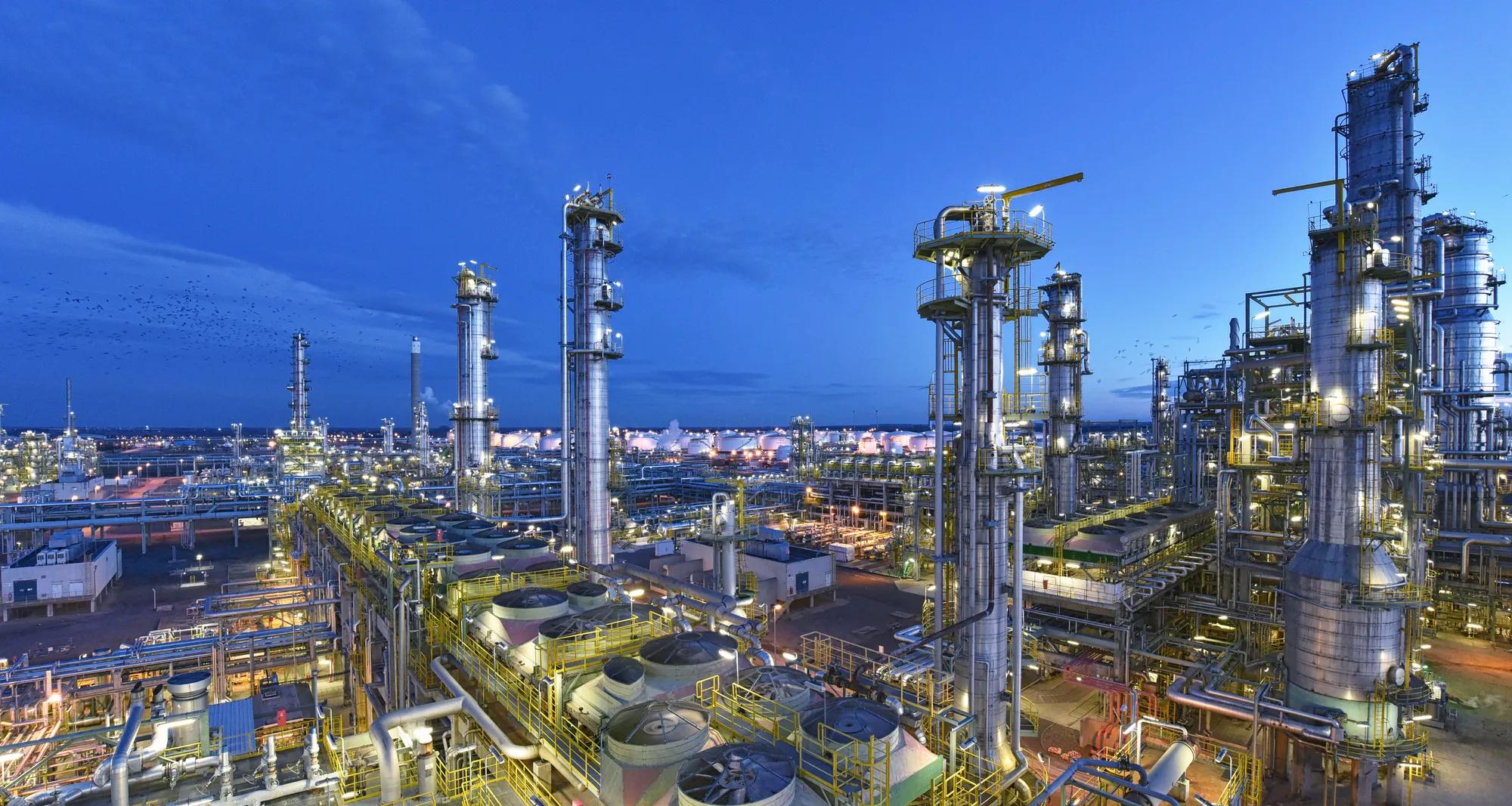 Illuminated oil and gas refinery at night with pipelines and industrial structures, representing critical infrastructure security and the need for advanced oil and gas industry protection