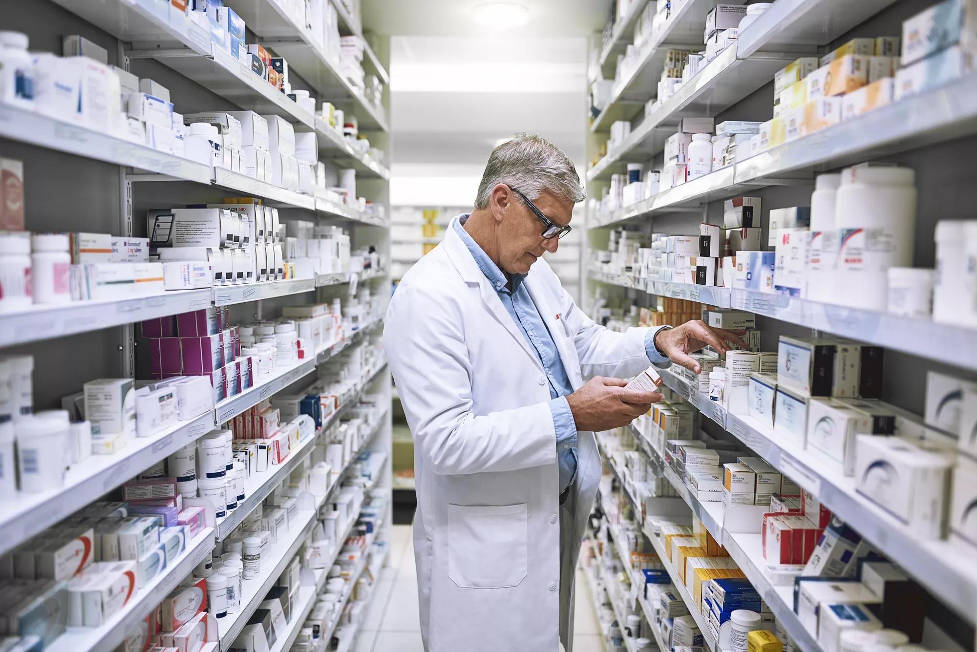 Pharmacy, medicine and search with man at shelf in drug store for thinking, inspection and inventory. Medical, healthcare and pills with senior male pharmacist for expert, wellness and product.