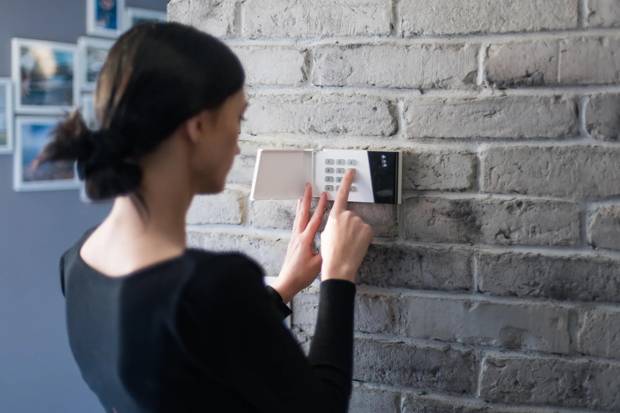 Young woman entering security pin on home alarm keypad. Home security system
