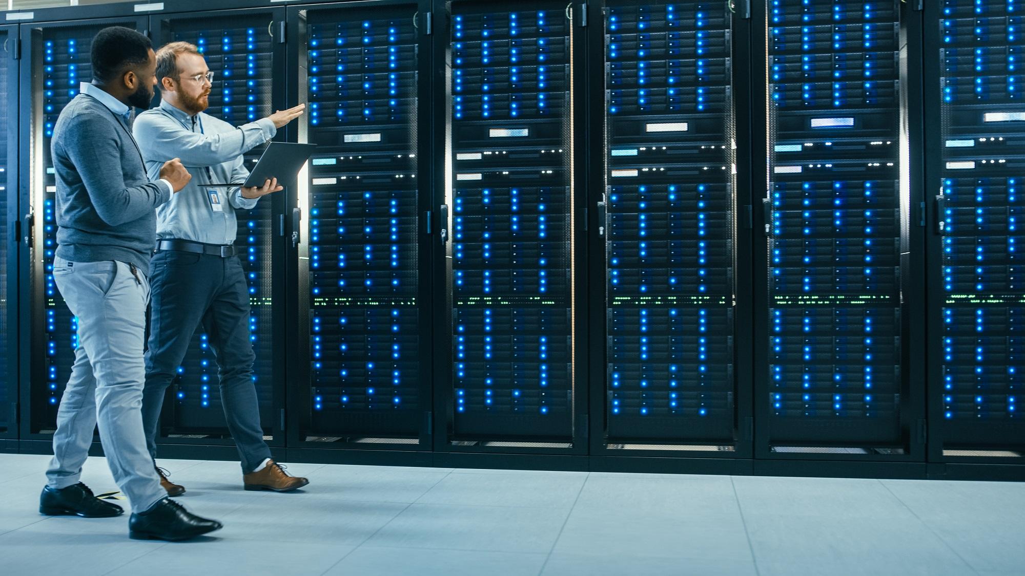 Two men walk next to wall of servers