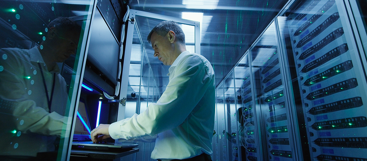 IT technician works at laptop in server room