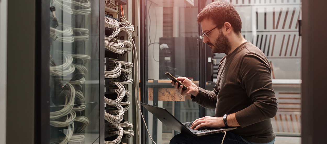 Man uses laptop in front of server bank