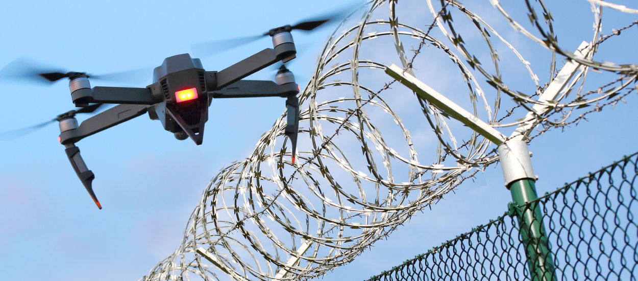 Drone flies next to top of barbed wire fence