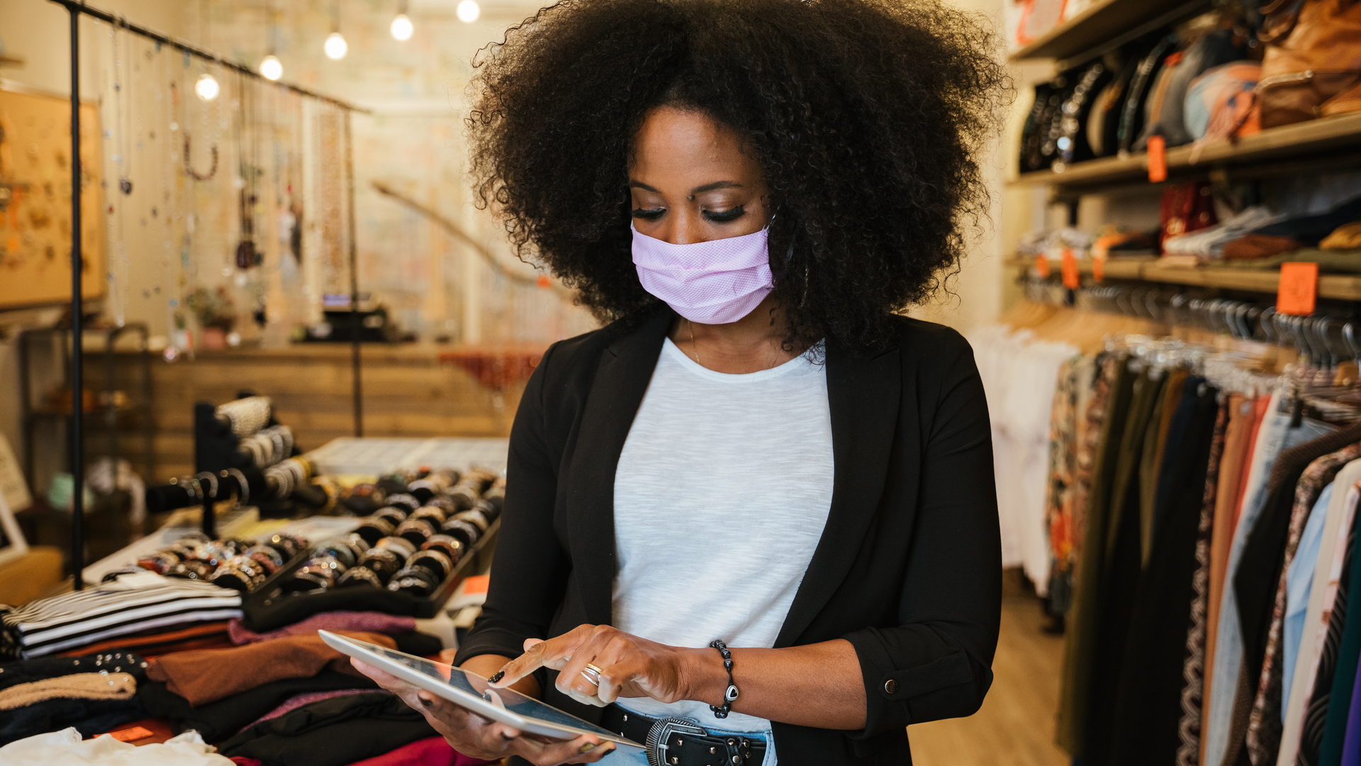 Clothing store owner wearing face mask uses tablet