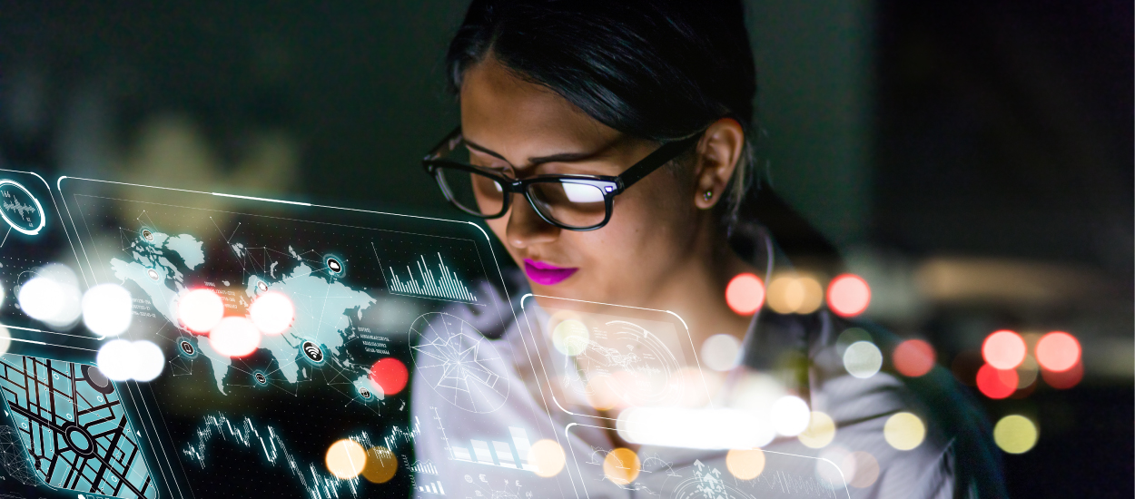 A woman with a dark ponytail and glasses and bright lipstick stares at a map on a futuristic glass screen