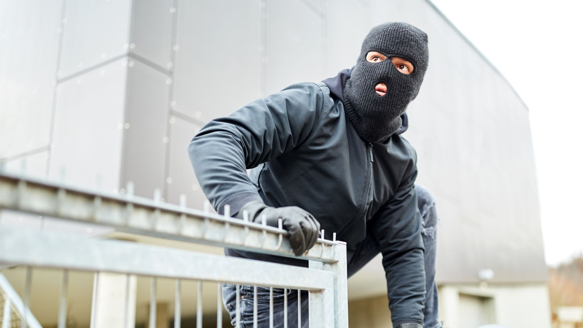 Person wearing black clothes and balaclava climbs fence