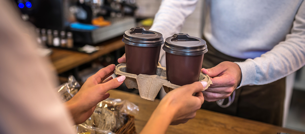 Barista hands customer coffee cups in a tray