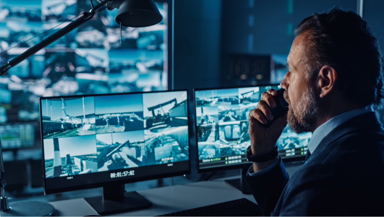 Male Officer Works on a Computer with Surveillance CCTV Video