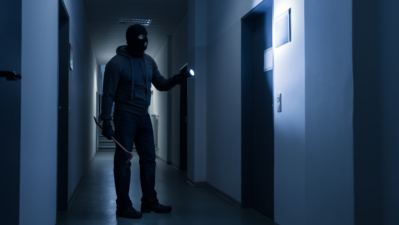 Full length of burglar with flashlight and crowbar in dark office building