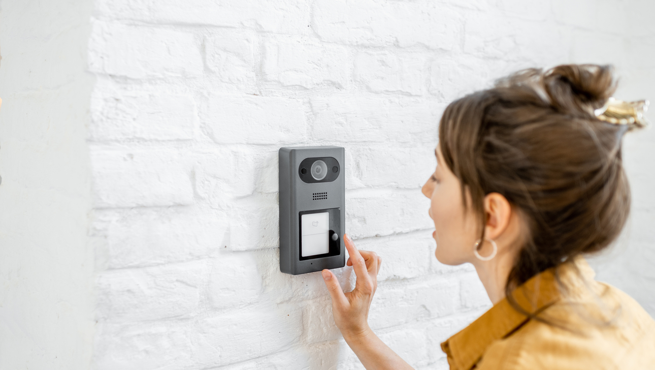 Woman rings the house intercom with a camera installed on the white brick wall