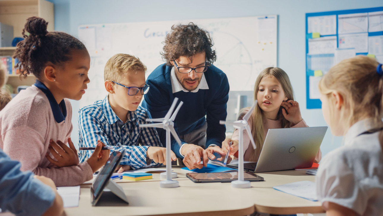 Enthusiastic Teacher Holding Tablet Computer Explains to a Brilliant Young Children How Wind Turbines Work