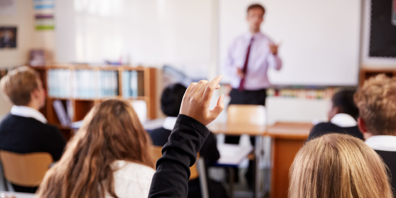 Female Student Raising Hand To Ask Question In Classroom