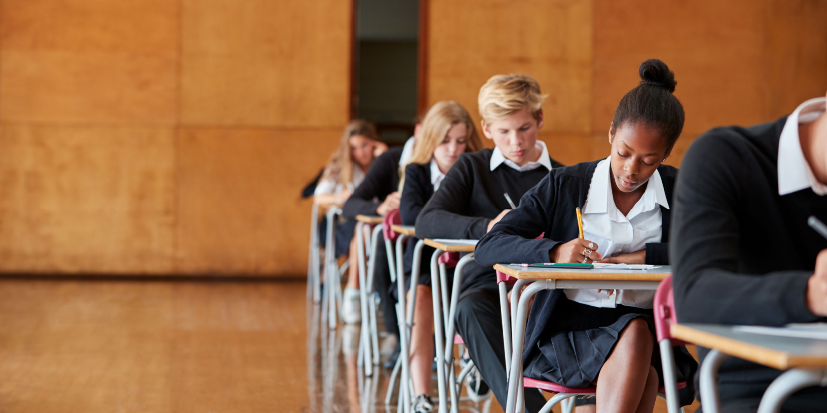 Teenage Students In Uniform Sitting Examination In School Hall