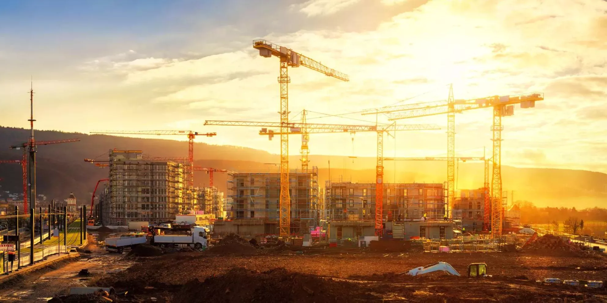 Large construction site including several cranes working on a building complex, illumined by warm gold sunlight