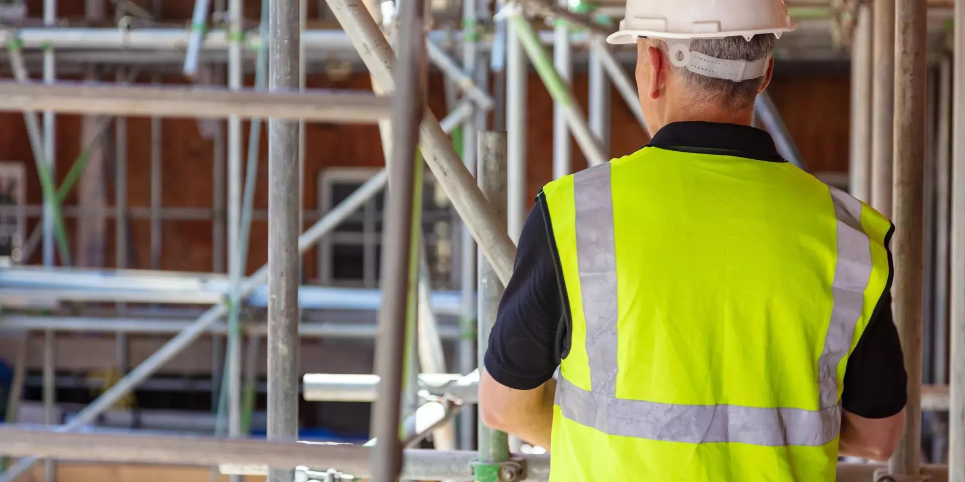 Rear view of male builder construction worker on building site wearing hard hat and hi-vis vest