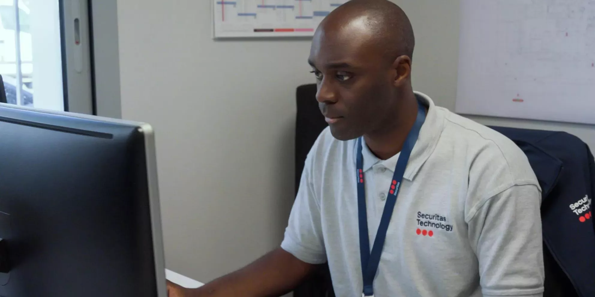A security professional working at a desktop in an office, with security system interfaces displayed on the screen, symbolizing professional and managed security services
