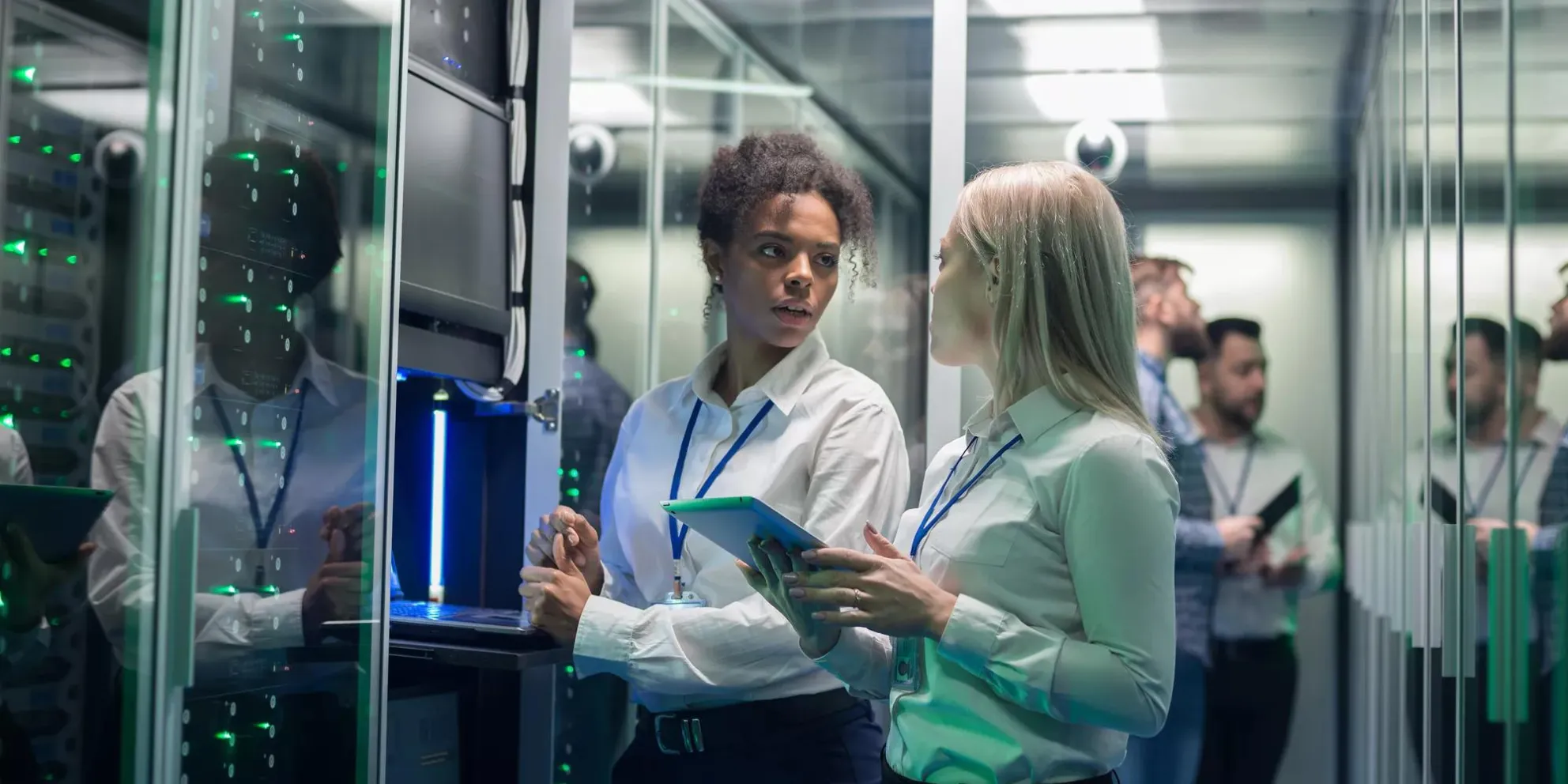 Medium shot of two women working in a data center with rows of server racks and checking the equipment and discussing their work
