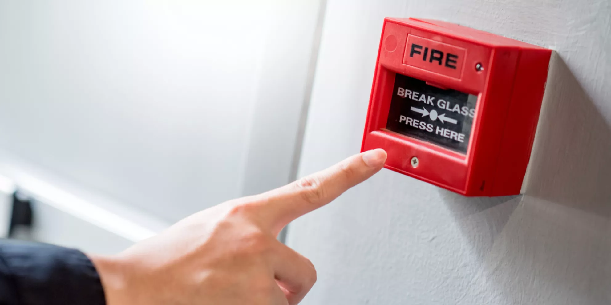 Male hand pointing at red fire alarm switch on concrete wall in office building