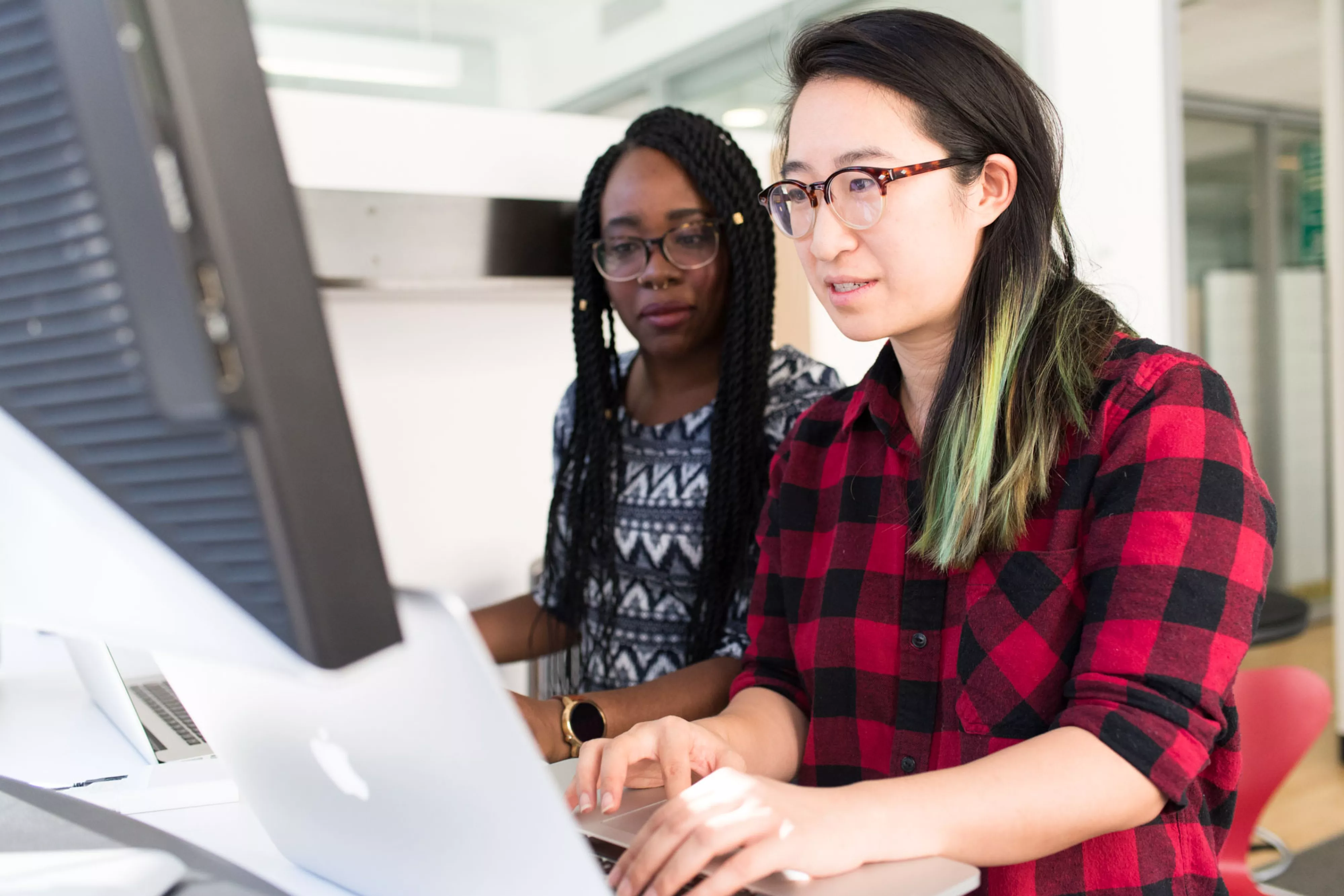 Two women use MacBook computer