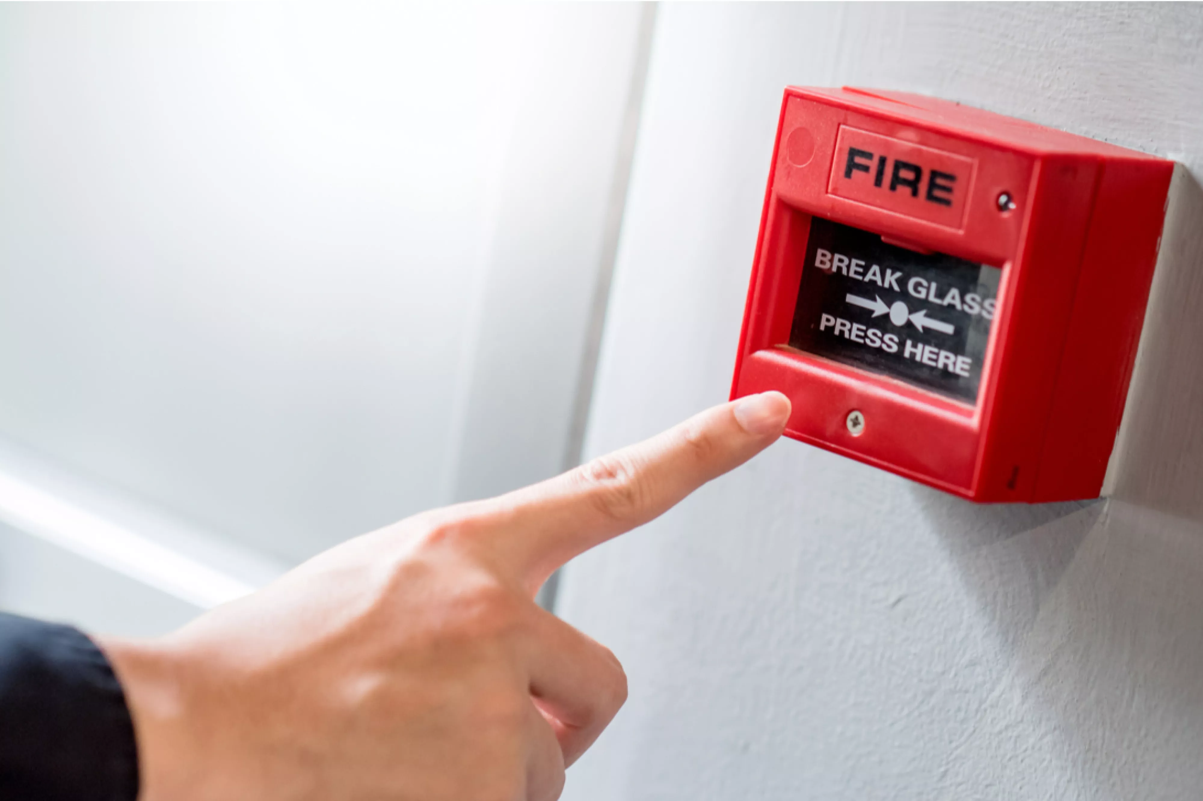 Male hand pointing at red fire alarm switch on concrete wall in office building