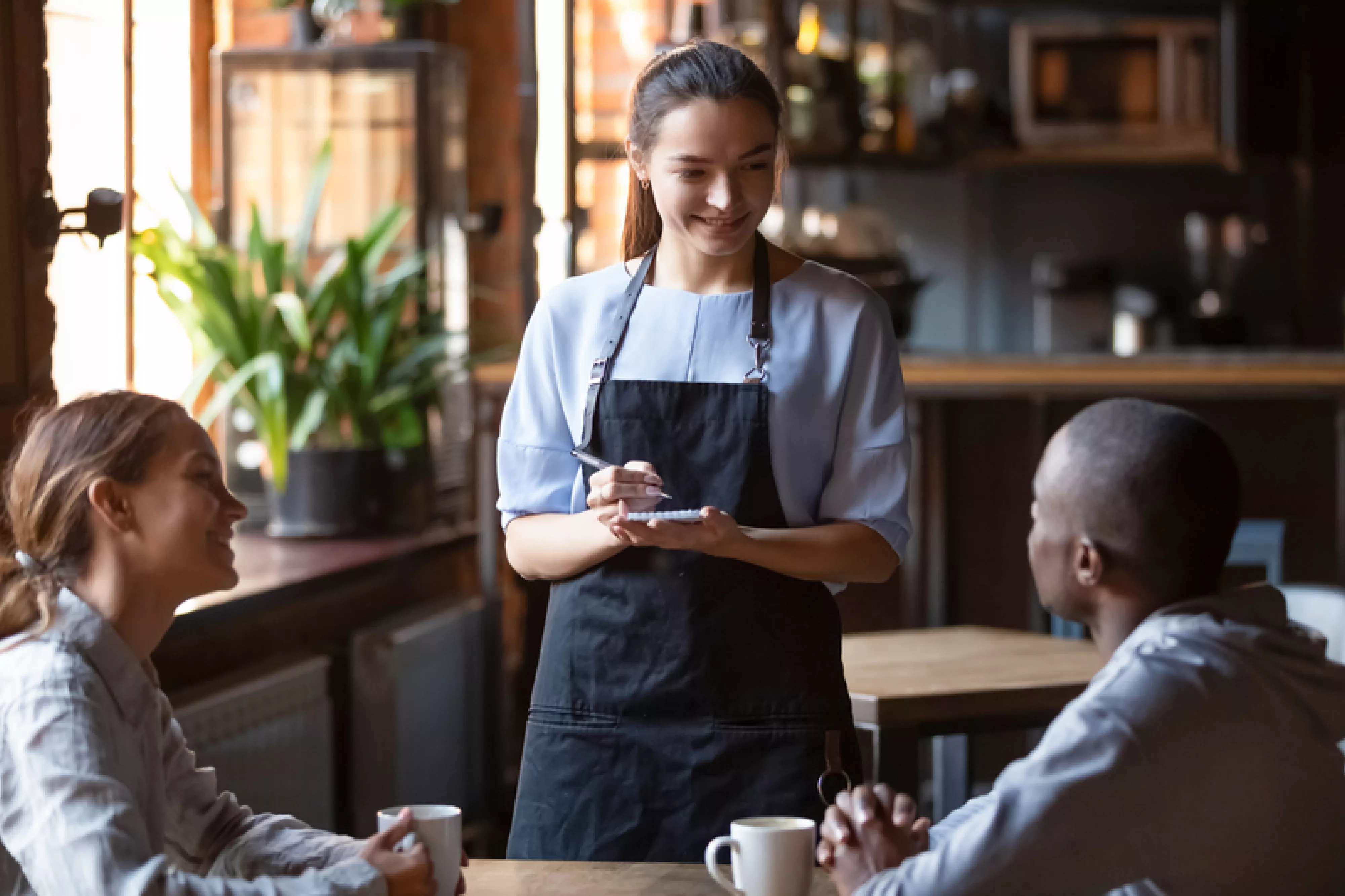 Waitress female welcoming diverse cafeteria pub guests african guy mixed race girl making order waiting staff writing wishes on notepad. Good service dining time, friends meets in public place concept