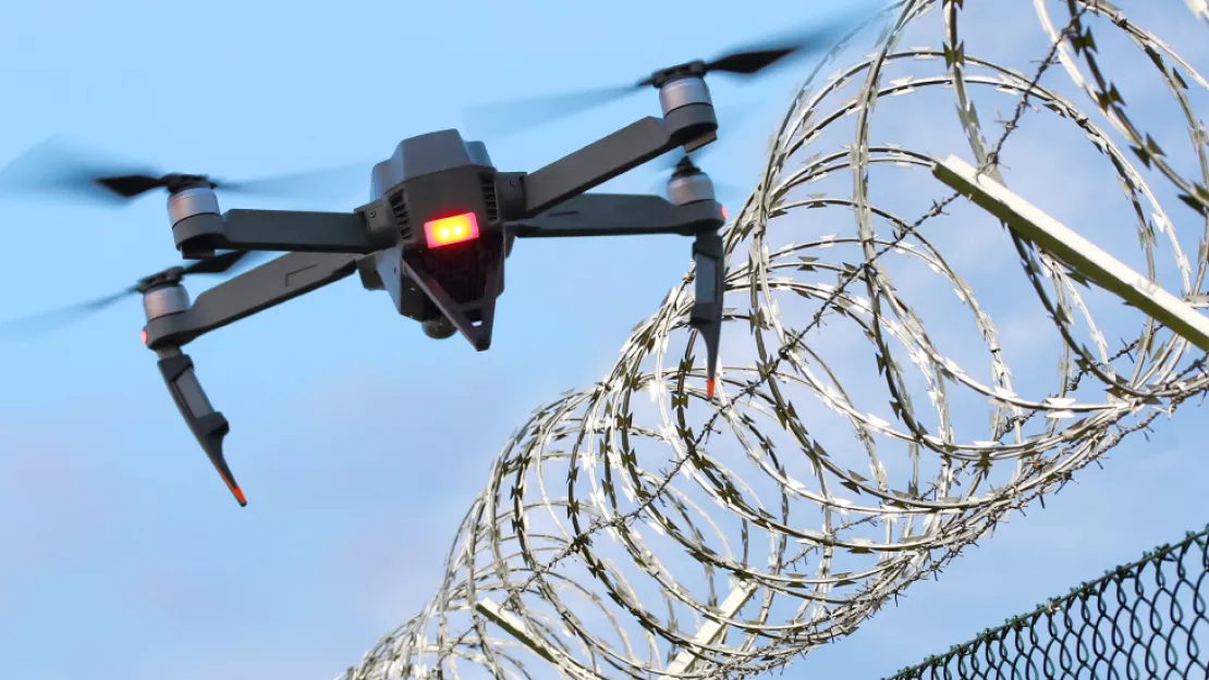 Drone flies next to top of barbed wire fence