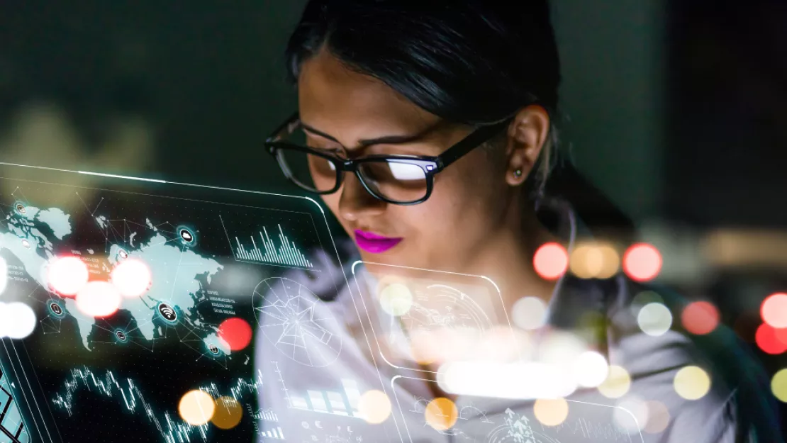A woman with a dark ponytail and glasses and bright lipstick stares at a map on a futuristic glass screen