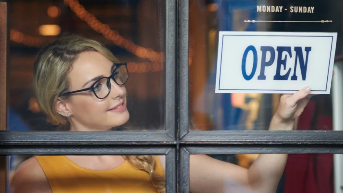 Smiling woman flips store window sign to open