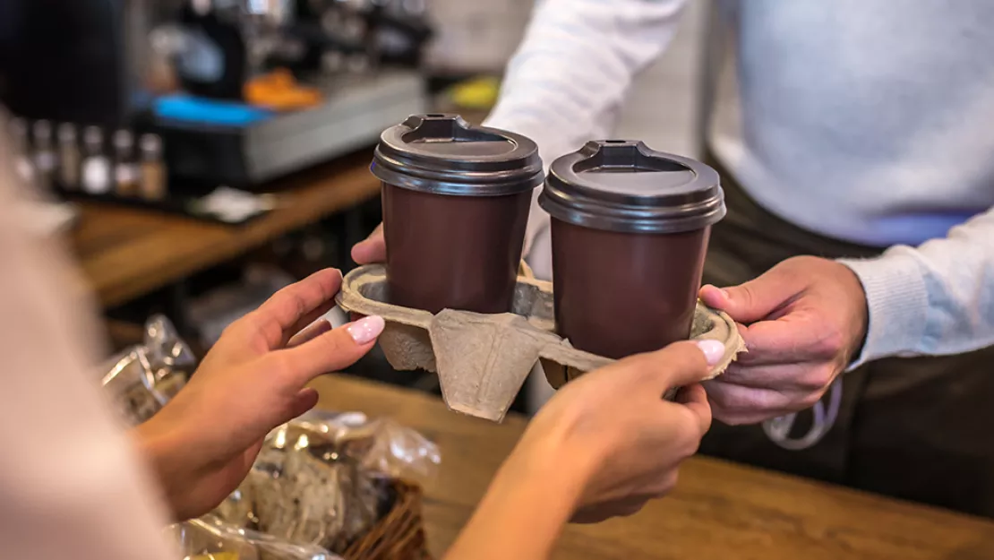 Barista hands customer coffee cups in a tray