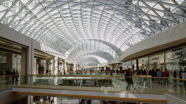 large multi-level shopping mall with various stores, escalators, and visible security measures, including a retail alarm system in place to protect the premises