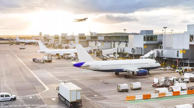 Busy airport view with airplanes and service vehicles at sunset. London airport with aircrafts at gates and taking off, trucks all around and sun setting on background. Travel and industry concepts