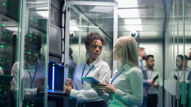 Medium shot of two women working in a data center with rows of server racks and checking the equipment and discussing their work