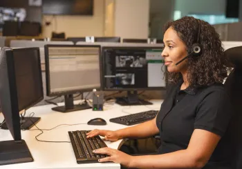 Säkerhetsövervakningspersonal som assisterar en kund via telefon från ett modernt övervakningscenter med brandlarmssystem