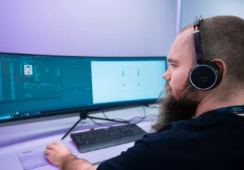 security monitoring professional sitting in front of a video surveillance monitoring system with multiple screens showing security camera feeds