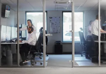 a professional security operator seated at a desk in a monitoring center, surrounded by multiple screens displaying live security camera feeds, system alerts, and analytics.