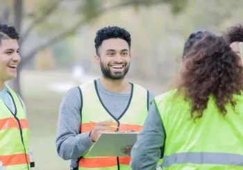 Confident young man talks with a group of male and female community volunteers. He is giving them instructions. They are wearing safety vests.