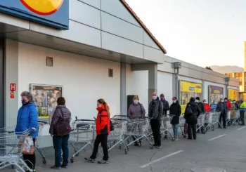 People in masks line up with carts outside grocery store