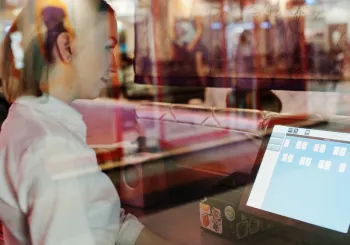 A woman behind glass stares at a computer screen