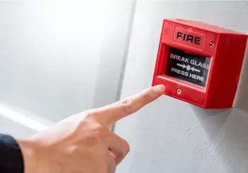 Male hand pointing at red fire alarm switch on concrete wall in office building