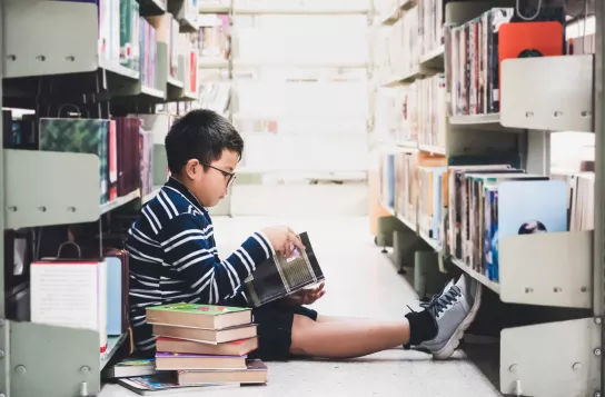 Boy sits on floor of library to read book