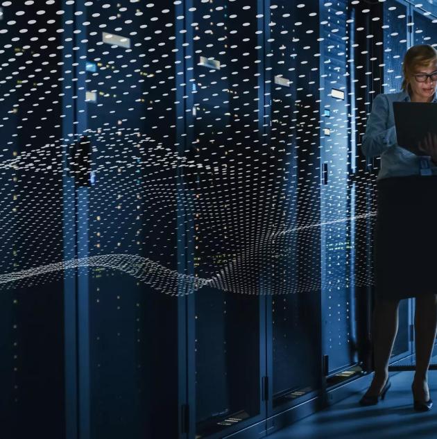 To personer i et datacenter står med en computer og taler sammen foran rackskabe	