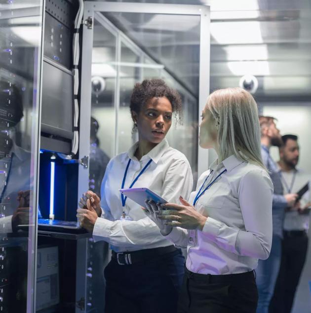 Medium shot of two women working in a data center with rows of server racks and checking the equipment and discussing their work