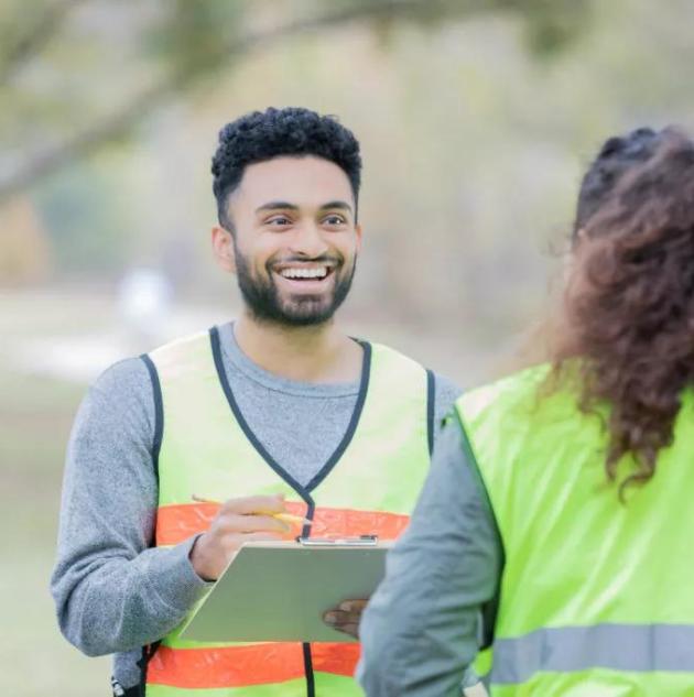 Confident young man talks with a group of male and female community volunteers. He is giving them instructions. They are wearing safety vests.