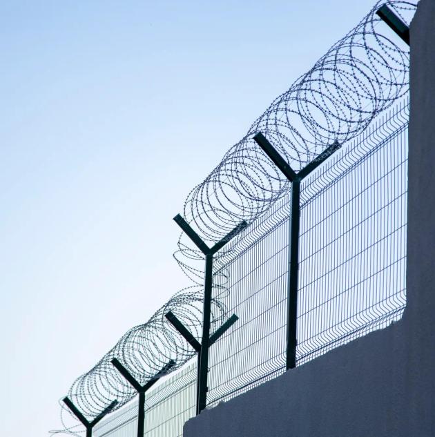 Steel grating fence of soccer field,Metal fence wire with bokeh in the background . Coiled razor wire with its sharp steel barbs on top of a wire mesh perimeter fence ensuring safety and security.