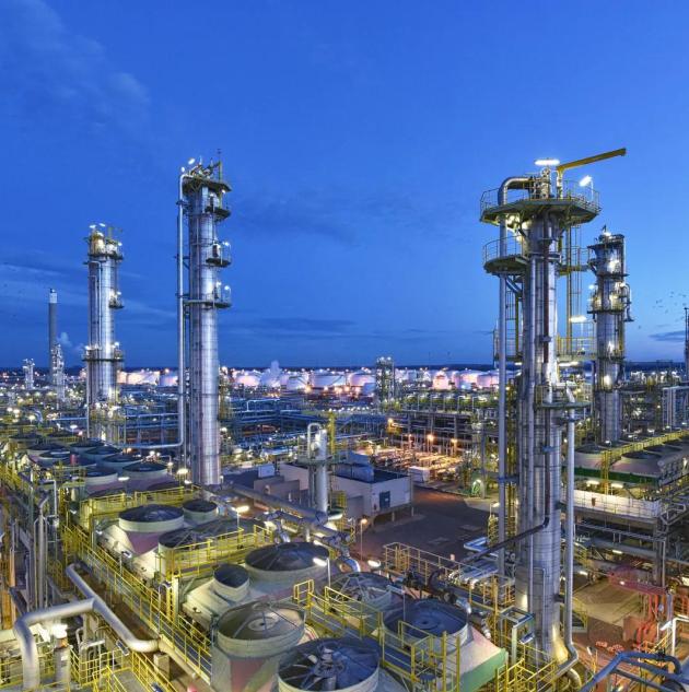 Illuminated oil and gas refinery at night with pipelines and industrial structures, representing critical infrastructure security and the need for advanced oil and gas industry protection